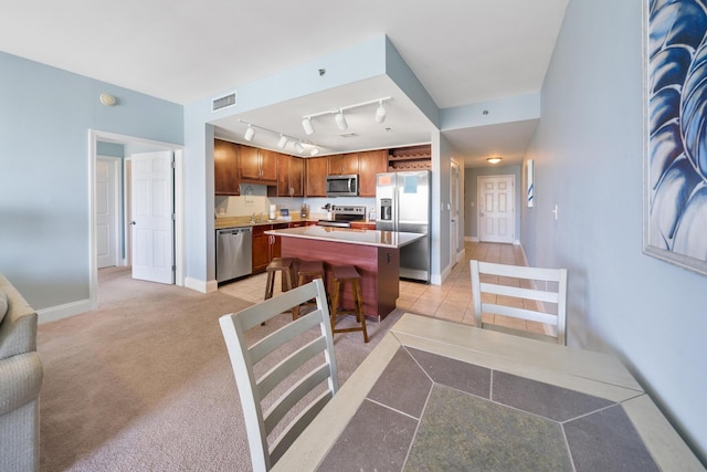 kitchen with stainless steel appliances, a breakfast bar, light countertops, a center island, and brown cabinetry