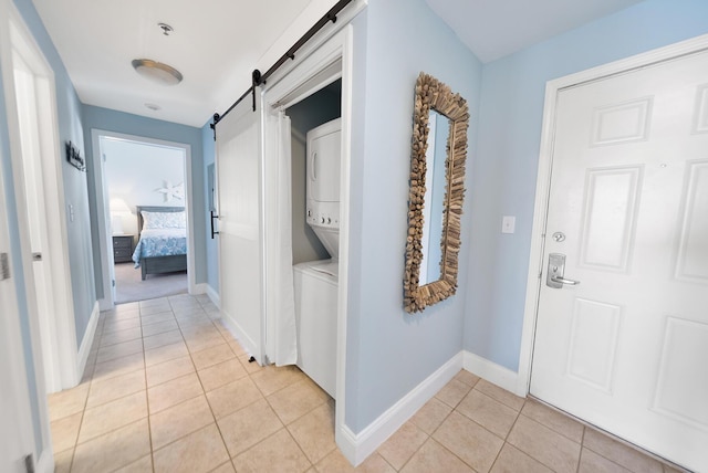 hall featuring light tile patterned floors, a barn door, baseboards, and stacked washer / drying machine