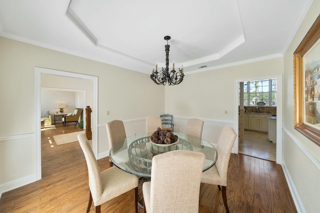 dining room with a notable chandelier, wood finished floors, baseboards, a tray ceiling, and crown molding