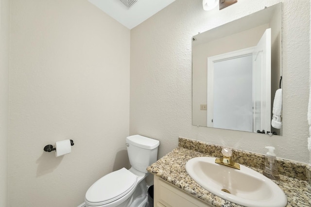 bathroom featuring toilet, a textured wall, visible vents, and vanity