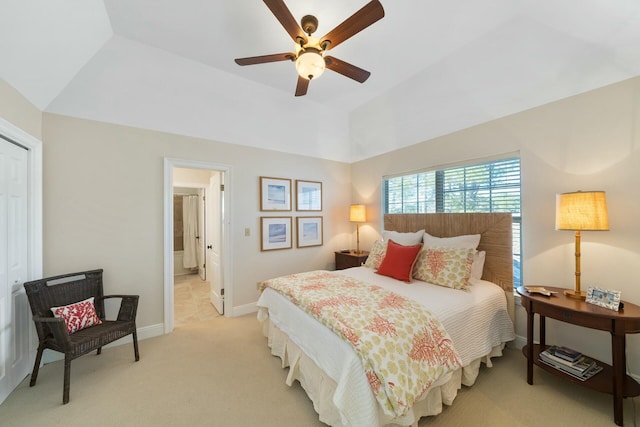 bedroom featuring ceiling fan, light colored carpet, baseboards, vaulted ceiling, and ensuite bath