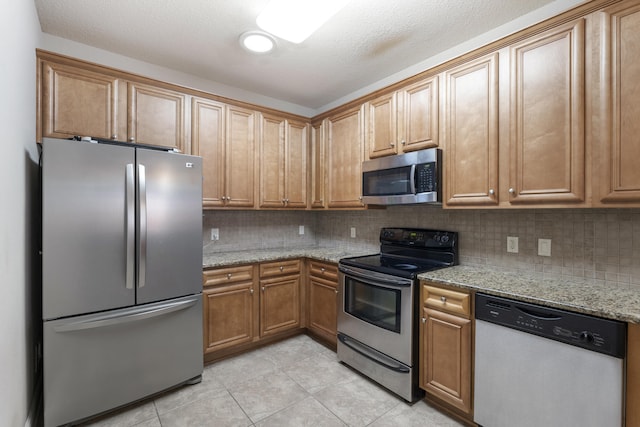 kitchen featuring appliances with stainless steel finishes, light stone counters, backsplash, and light tile patterned flooring