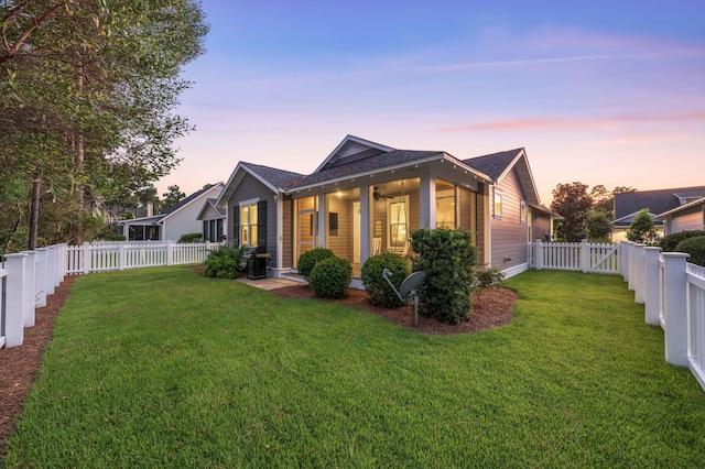 back of house at dusk with ceiling fan, a yard, and a fenced backyard