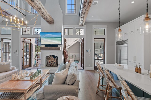 living room featuring a notable chandelier, a high ceiling, wood finished floors, baseboards, and a lit fireplace