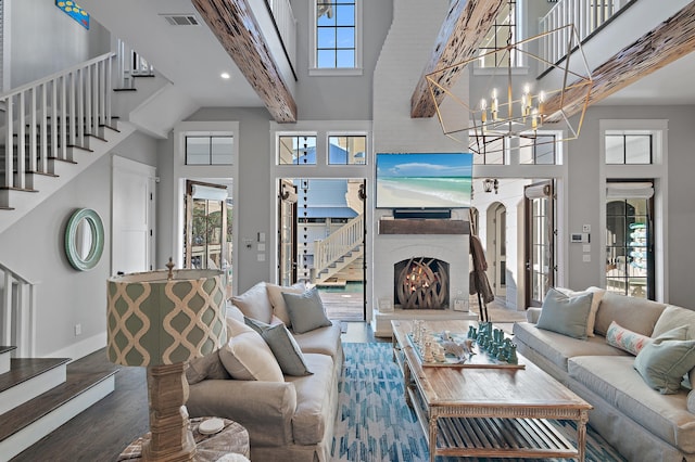 living room featuring visible vents, a high ceiling, an inviting chandelier, a warm lit fireplace, and stairs