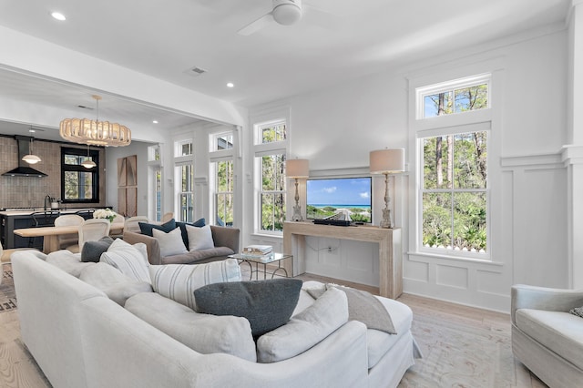 living area with light wood-style floors, recessed lighting, a decorative wall, and ceiling fan with notable chandelier