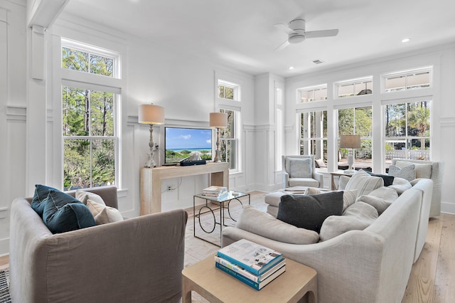 living room featuring ceiling fan, light wood-style flooring, a decorative wall, a wainscoted wall, and visible vents