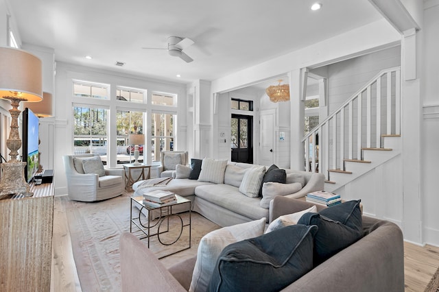 living area featuring visible vents, a ceiling fan, light wood-style flooring, stairway, and a decorative wall