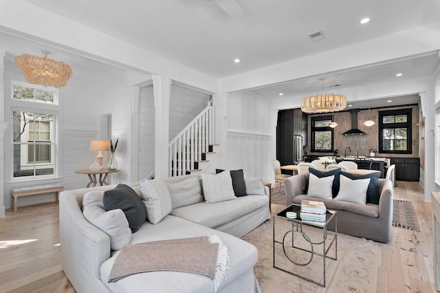 living room with light wood-style floors, a healthy amount of sunlight, visible vents, and stairs