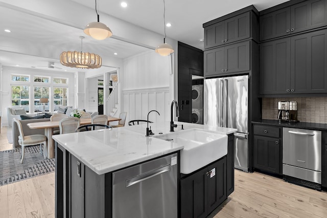 kitchen with a center island with sink, stacked washer / drying machine, hanging light fixtures, stainless steel appliances, and dark cabinetry