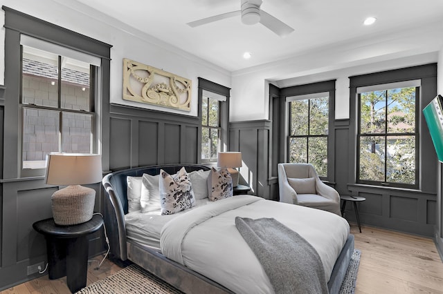 bedroom featuring light wood-style flooring, a decorative wall, crown molding, and recessed lighting