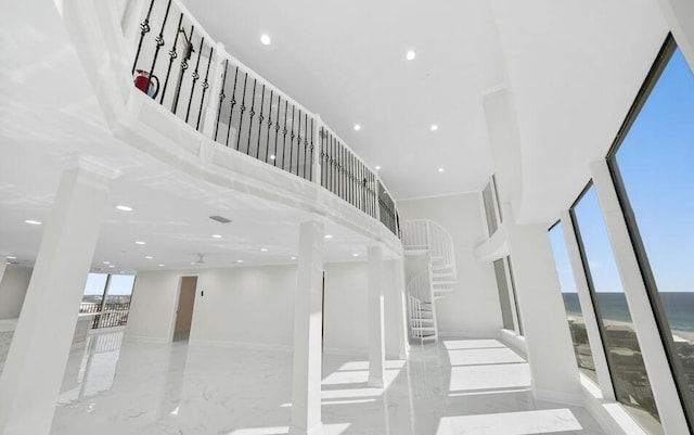 stairs with recessed lighting, marble finish floor, a water view, and a towering ceiling