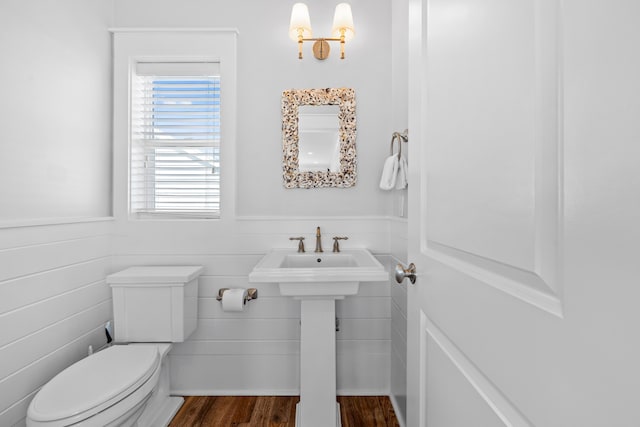 half bath featuring toilet, a sink, wood finished floors, and wainscoting