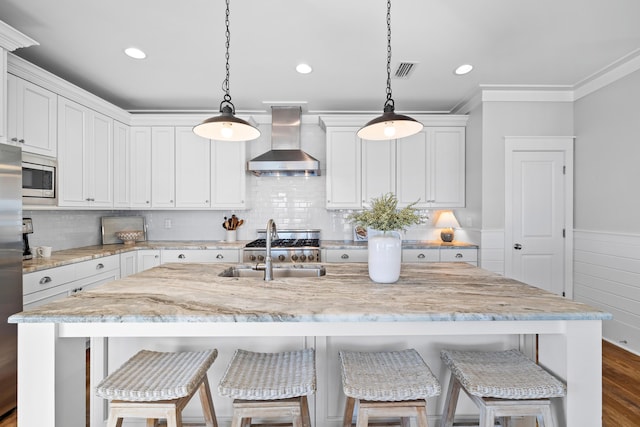 kitchen with appliances with stainless steel finishes, extractor fan, a center island with sink, and white cabinets