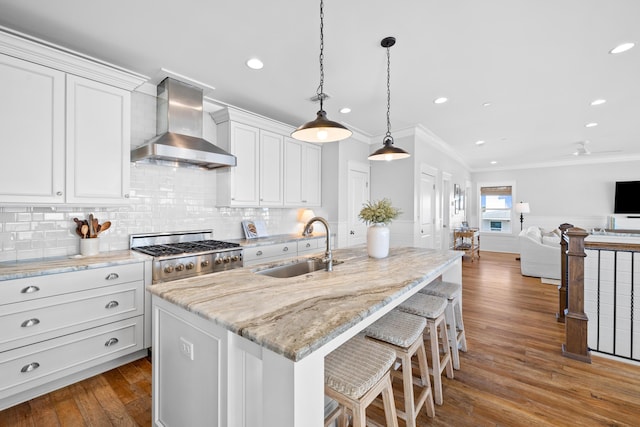 kitchen with a kitchen island with sink, open floor plan, white cabinetry, and wall chimney range hood