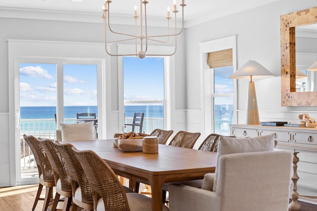 dining area featuring a chandelier, a water view, ornamental molding, and light wood-style flooring