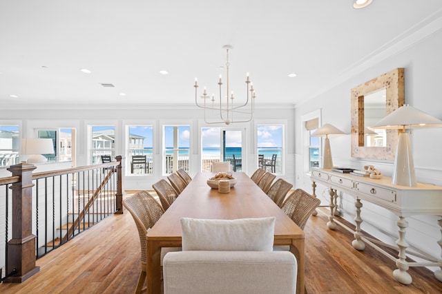 dining room featuring ornamental molding, wood finished floors, a water view, and an inviting chandelier