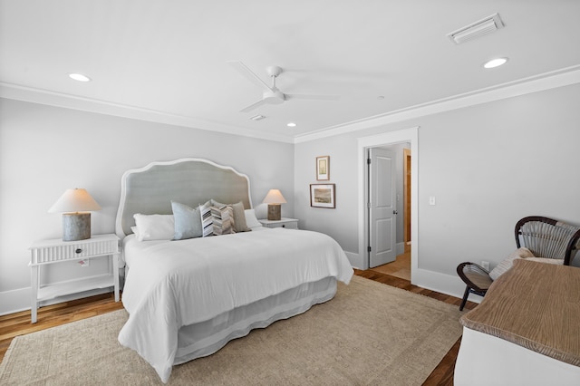 bedroom with baseboards, crown molding, visible vents, and wood finished floors