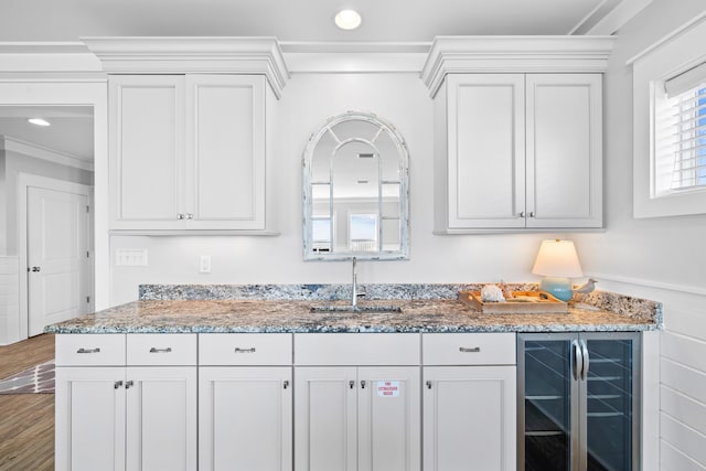 kitchen with wood finished floors, wine cooler, a sink, and white cabinets