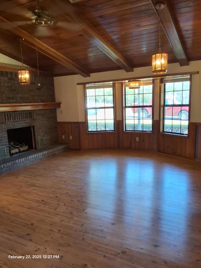 unfurnished living room featuring a wainscoted wall, beamed ceiling, wood ceiling, and a healthy amount of sunlight