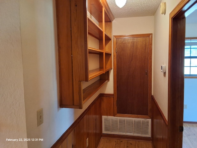 interior space with light wood finished floors, visible vents, wainscoting, wood walls, and a textured ceiling