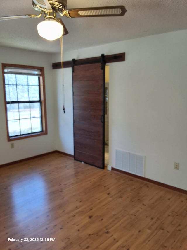 spare room with a ceiling fan, a barn door, visible vents, and wood finished floors