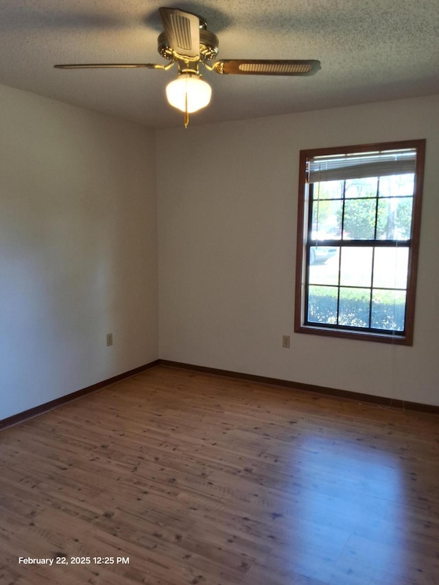 empty room with ceiling fan, a textured ceiling, baseboards, and wood finished floors