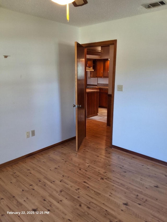 unfurnished room with light wood finished floors, baseboards, visible vents, and a textured ceiling