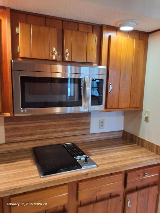 kitchen with brown cabinets, light countertops, stainless steel microwave, and gas stovetop