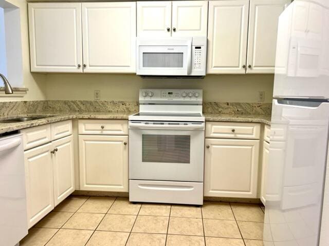 kitchen featuring light tile patterned floors, light stone counters, white appliances, a sink, and white cabinetry