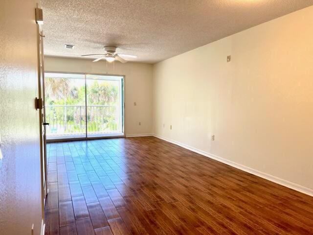 empty room featuring a textured ceiling, visible vents, a ceiling fan, baseboards, and dark wood finished floors