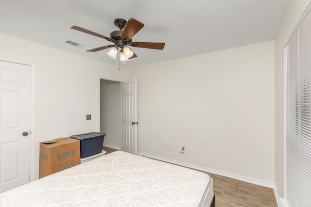 bedroom featuring a ceiling fan, wood finished floors, visible vents, and baseboards