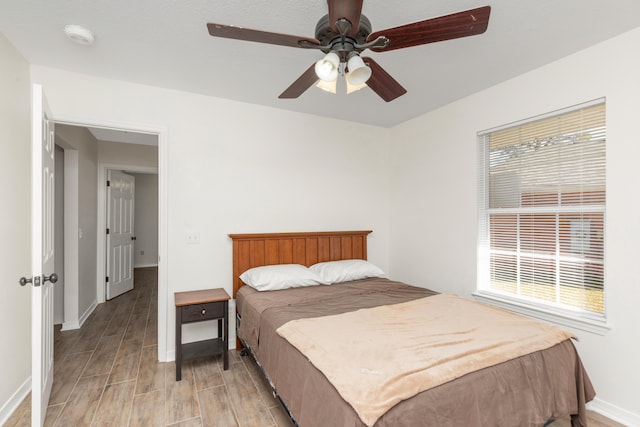 bedroom with a ceiling fan, multiple windows, light wood-style flooring, and baseboards