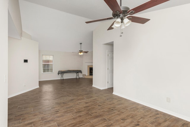 unfurnished living room featuring a fireplace with raised hearth, ceiling fan, lofted ceiling, baseboards, and dark wood finished floors