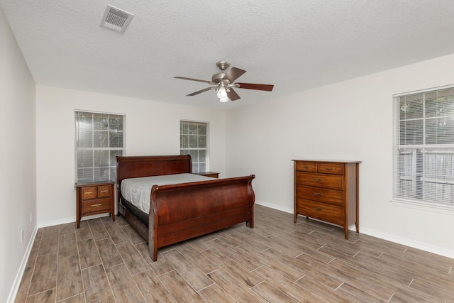 bedroom with a textured ceiling, wood finish floors, visible vents, and baseboards