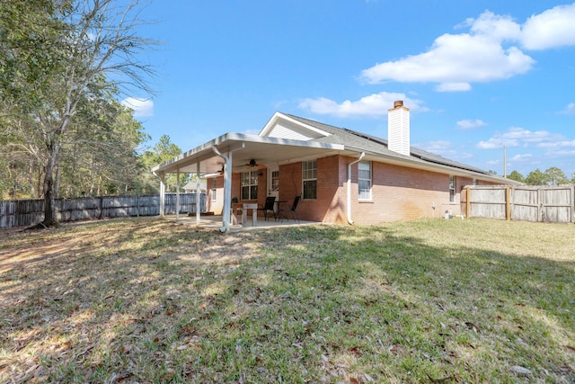 back of house featuring a fenced backyard, brick siding, a lawn, a chimney, and a patio area