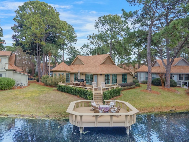 back of house with a shingled roof, outdoor dining area, a water view, and a yard