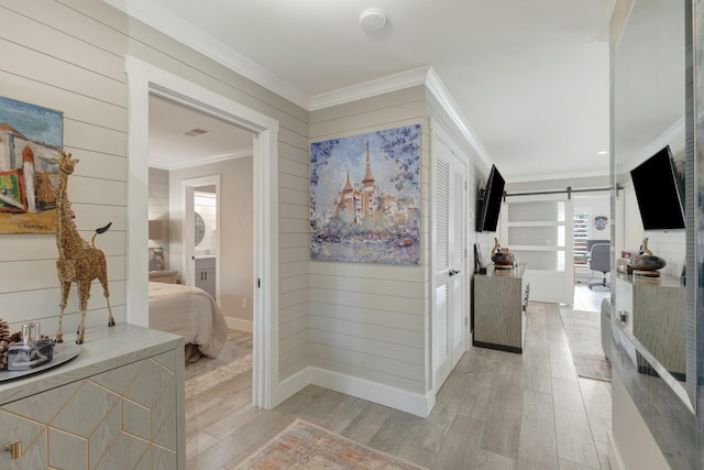 hall with crown molding, visible vents, a barn door, light wood-style floors, and wood walls