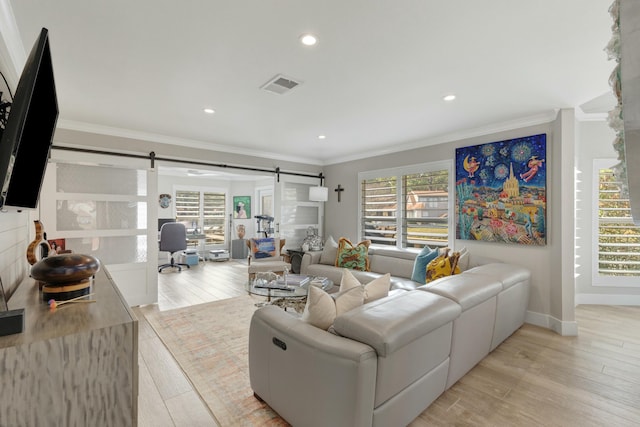 living area featuring a barn door, visible vents, a healthy amount of sunlight, crown molding, and light wood-type flooring