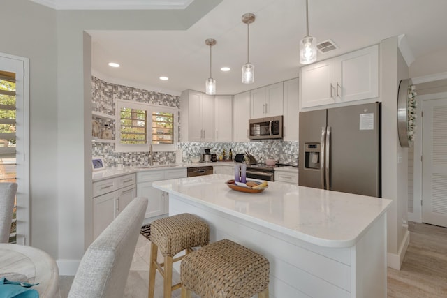 kitchen featuring appliances with stainless steel finishes, a center island, white cabinetry, and decorative light fixtures