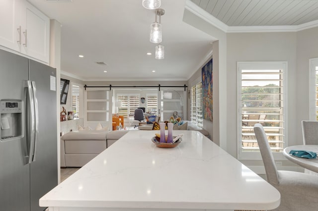 kitchen featuring a barn door, light stone counters, white cabinets, stainless steel fridge with ice dispenser, and decorative light fixtures