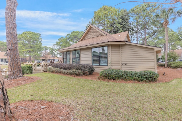 view of side of property with a shingled roof, a lawn, and a deck