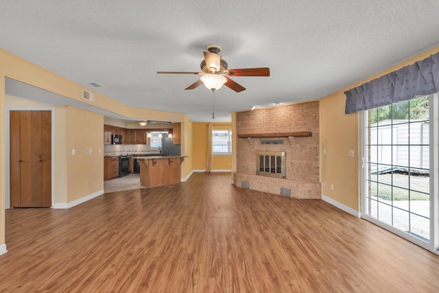 unfurnished living room featuring plenty of natural light, light wood-type flooring, visible vents, and a brick fireplace