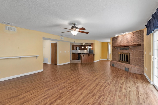 unfurnished living room with visible vents, a ceiling fan, a brick fireplace, a textured ceiling, and wood finished floors