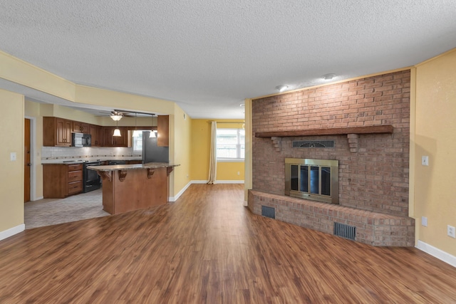 unfurnished living room featuring a brick fireplace, visible vents, ceiling fan, and wood finished floors