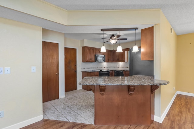 kitchen with ceiling fan, a peninsula, backsplash, black appliances, and a kitchen bar