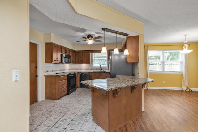 kitchen with a ceiling fan, a sink, black appliances, a peninsula, and a kitchen breakfast bar