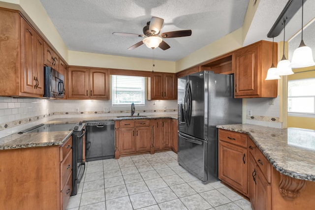 kitchen with brown cabinetry, dark stone countertops, a sink, and black appliances