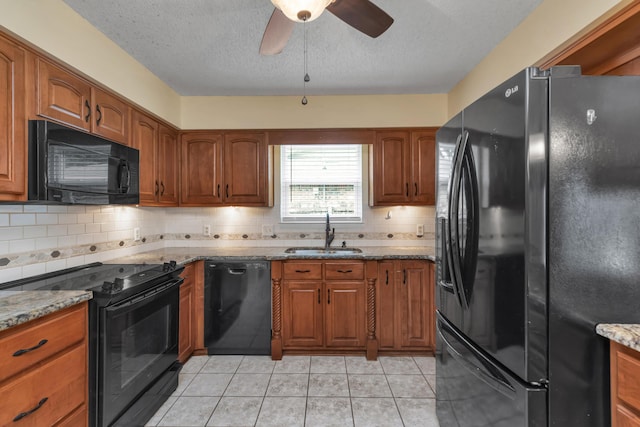 kitchen featuring black appliances, light stone counters, brown cabinetry, and a sink