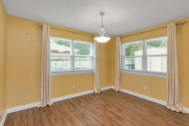 spare room with a healthy amount of sunlight, a textured ceiling, baseboards, and wood finished floors